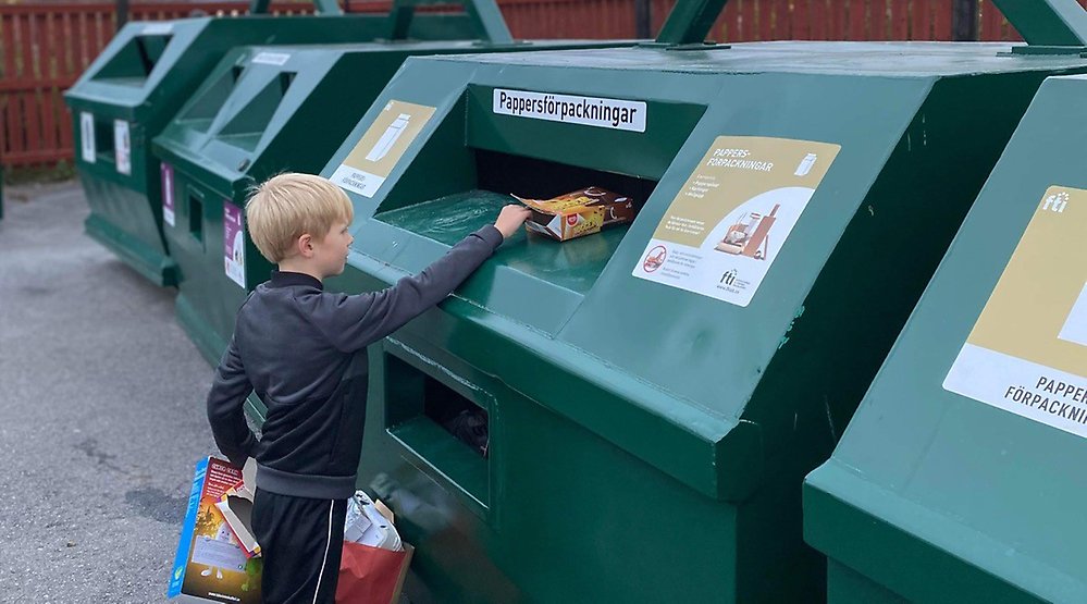 Pojke sorterar förpackningar vid återvinningsstation